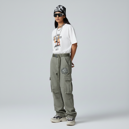 Person wearing a white graphic t-shirt, green cargo pants, and a black cap on a gray background